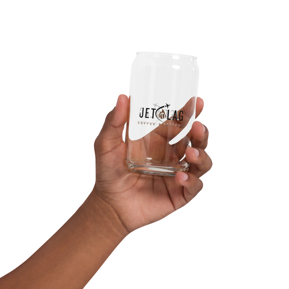 The image shows a hand holding a clear glass shaped like a soda can. The glass features the logo for "Jet Lag Coffee Roasters," which includes the text "JET LAG" with two small airplanes and a stylized coffee bean and flame. Below the main logo, the words "COFFEE ROASTERS" are printed. The glass is empty, and the hand is positioned against a white background.